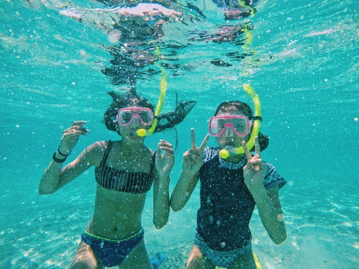Family with children smiling and snorkeling in shallow, clear turquoise water